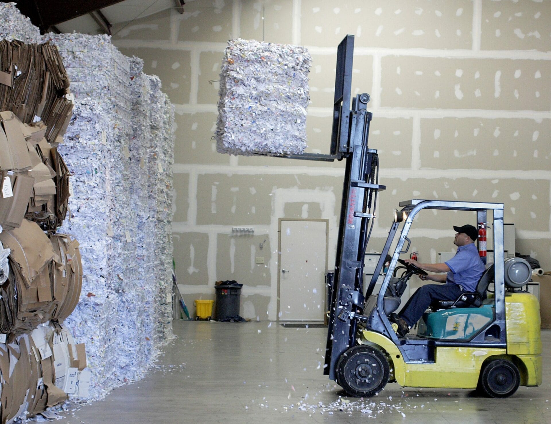 Forklift moving stacked cardboard bales in warehouse
