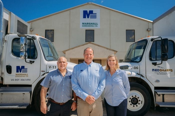 Three people standing between company trucks.
