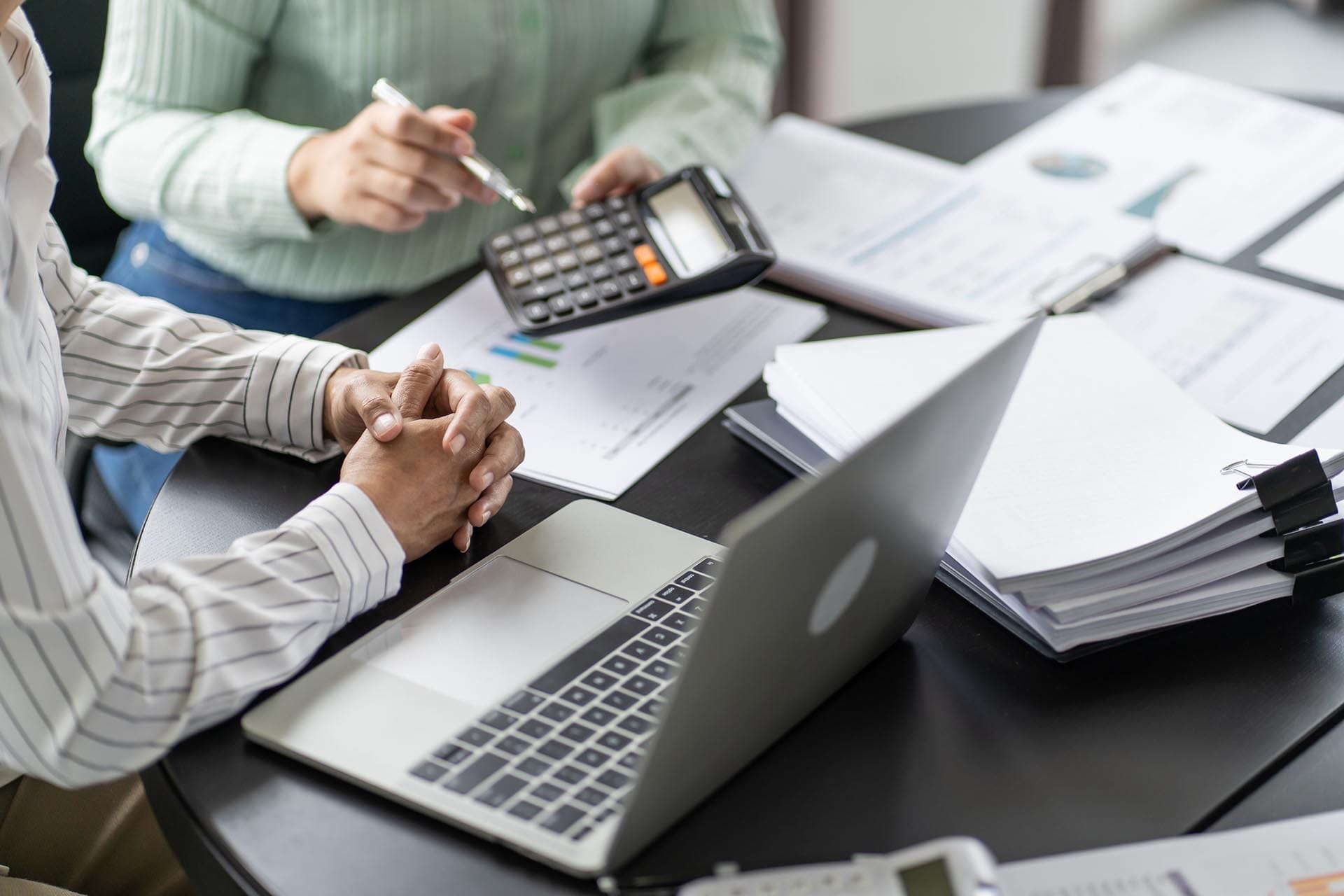 Two people discussing finances with documents, calculator, laptop.